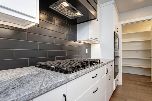 kitchen featuring black gas cooktop, exhaust hood, oven, and white cabinets