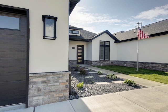 entrance to property with stucco siding, stone siding, and a shingled roof