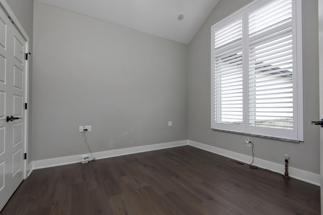 spare room featuring vaulted ceiling, dark wood finished floors, and baseboards