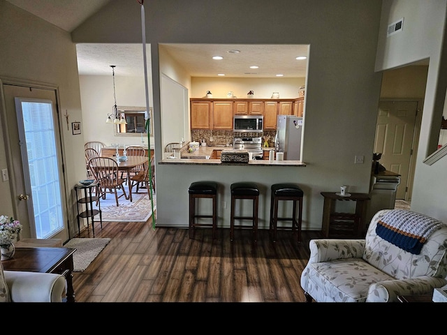 71 Birdie Ln Unit 3, Branson West, MO 65737 - kitchen with appliances with stainless steel finishes, dark wood-style flooring, backsplash, a kitchen breakfast bar, and brown cabinetry