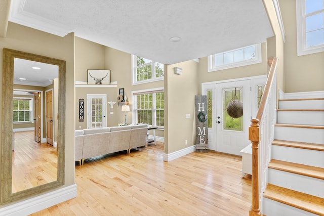 foyer with light wood-style flooring, stairs, ornamental molding, baseboards, and plenty of natural light
