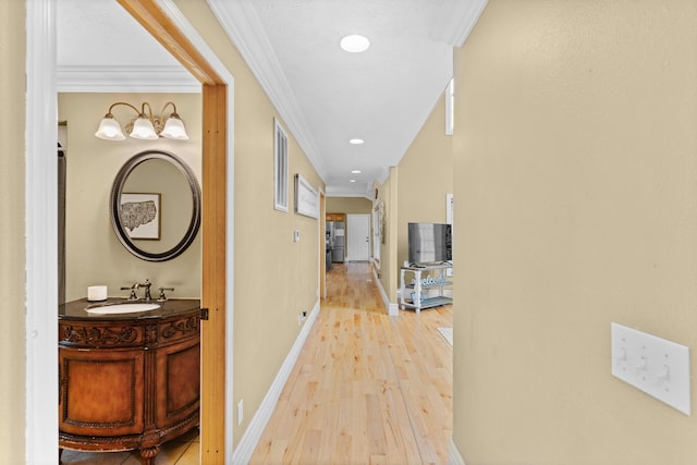 hall with a sink, light wood-style floors, ornamental molding, and baseboards