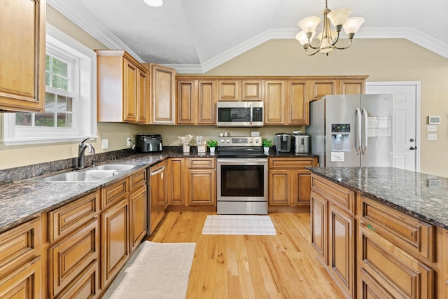 kitchen with appliances with stainless steel finishes, a sink, vaulted ceiling, brown cabinets, and light wood-type flooring
