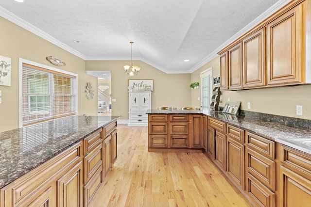 kitchen featuring light wood-type flooring, brown cabinets, a peninsula, a textured ceiling, and vaulted ceiling