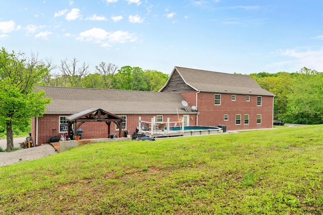 back of house featuring a gazebo, brick siding, an outdoor pool, and a yard
