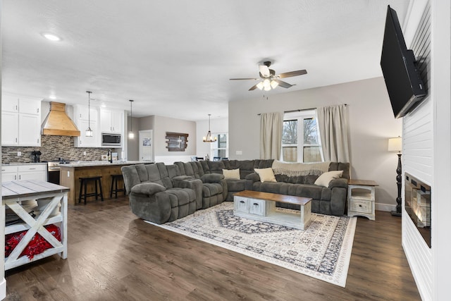 living area with a ceiling fan, a glass covered fireplace, dark wood-style floors, a chandelier, and baseboards