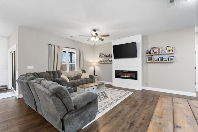 living area with ceiling fan, dark wood-style floors, baseboards, and a large fireplace