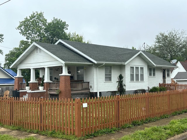 view of front of home with a porch, a fenced front yard, and a shingled roof