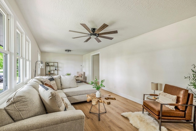 living area with a textured ceiling, light wood-style flooring, a ceiling fan, baseboards, and healthy amount of natural light