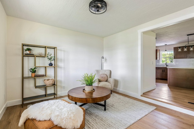 living area featuring light wood-style flooring, baseboards, and a textured ceiling