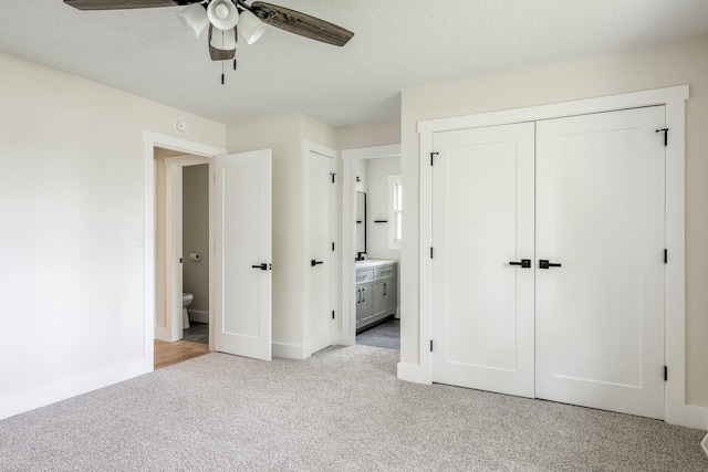 unfurnished bedroom featuring light colored carpet, ensuite bath, baseboards, and a ceiling fan