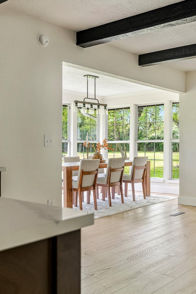 dining area featuring a textured wall, beamed ceiling, wood finished floors, and baseboards