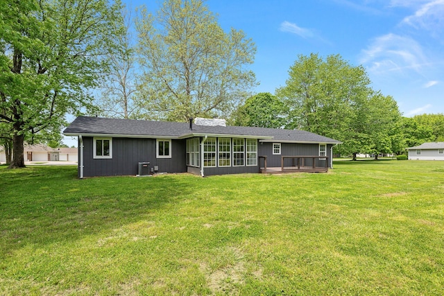 back of property with cooling unit, a sunroom, a lawn, a deck, and roof with shingles