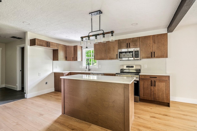 kitchen featuring stainless steel appliances, light wood-style floors, baseboards, a kitchen island, and light countertops