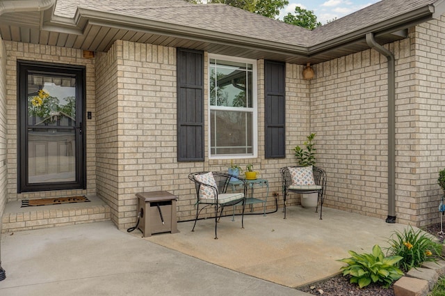 doorway to property featuring a shingled roof and brick siding