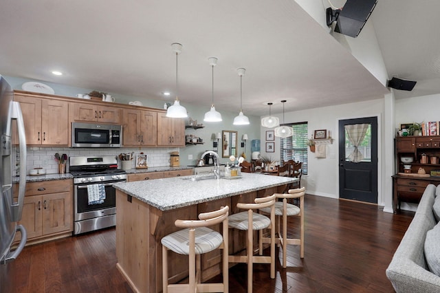 kitchen with stainless steel appliances, a sink, backsplash, a breakfast bar, and dark wood-style floors