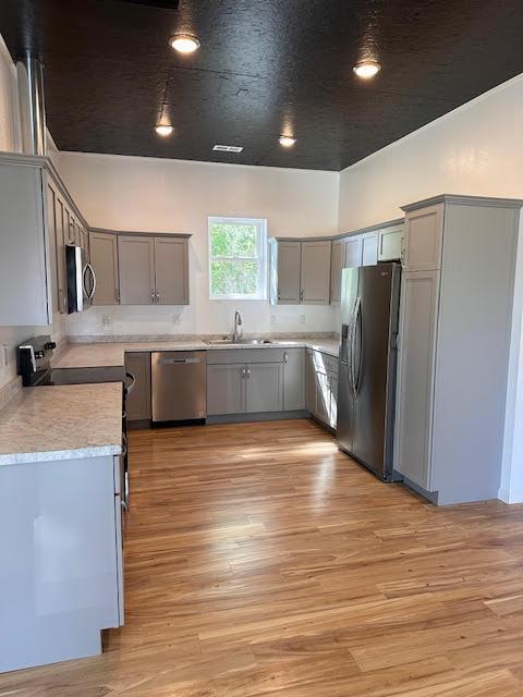 kitchen with stainless steel appliances, gray cabinetry, a sink, light wood-style floors, and recessed lighting