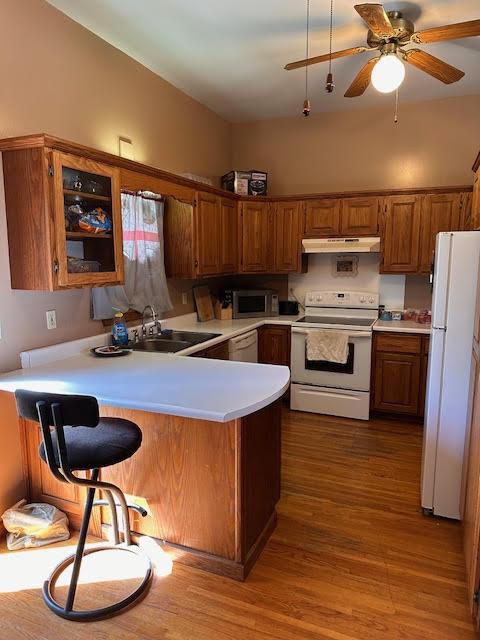 kitchen with white appliances, a sink, a peninsula, light countertops, and brown cabinetry