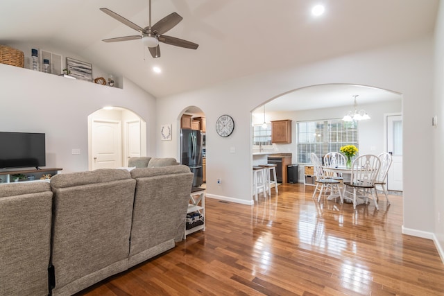 living room with a ceiling fan, light wood-style floors, arched walkways, baseboards, and high vaulted ceiling