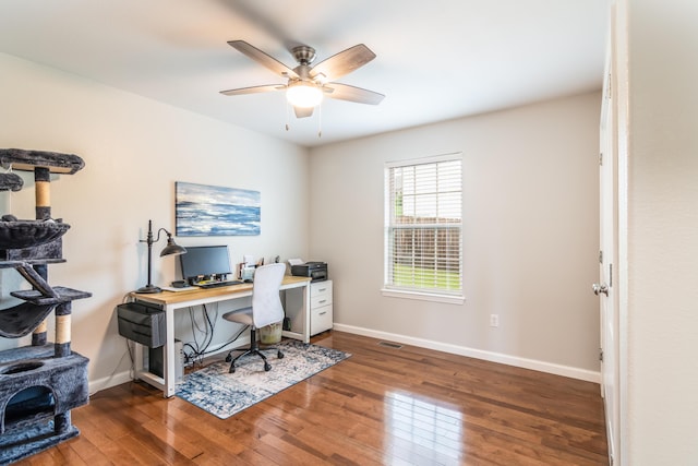 office space with a wood stove, wood-type flooring, ceiling fan, and baseboards
