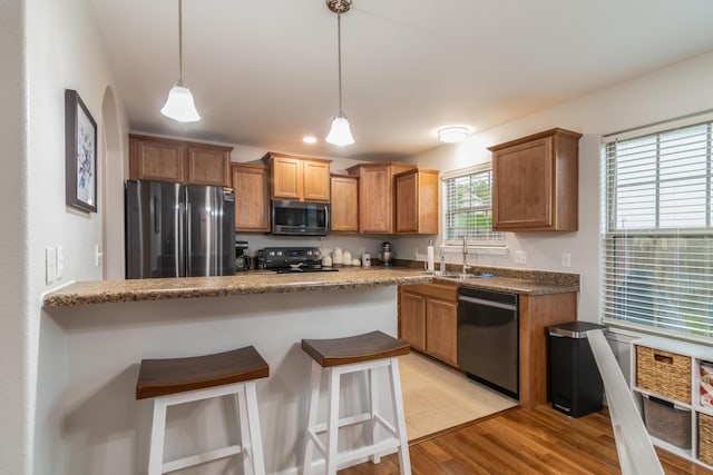 kitchen featuring appliances with stainless steel finishes, a sink, a breakfast bar, hanging light fixtures, and light wood finished floors