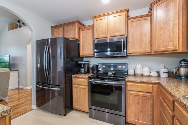 kitchen featuring stainless steel appliances, arched walkways, and light stone countertops