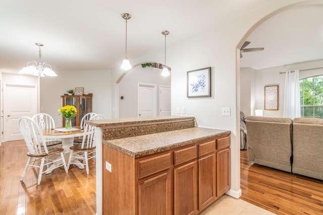 kitchen with arched walkways, light wood finished floors, brown cabinetry, and decorative light fixtures