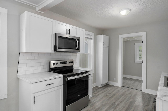 kitchen featuring stainless steel appliances, decorative backsplash, light wood-style floors, white cabinetry, and baseboards
