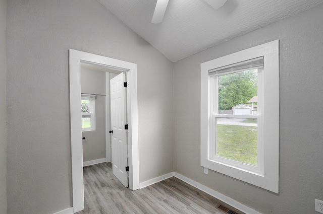 spare room with light wood finished floors, lofted ceiling, healthy amount of natural light, and ceiling fan