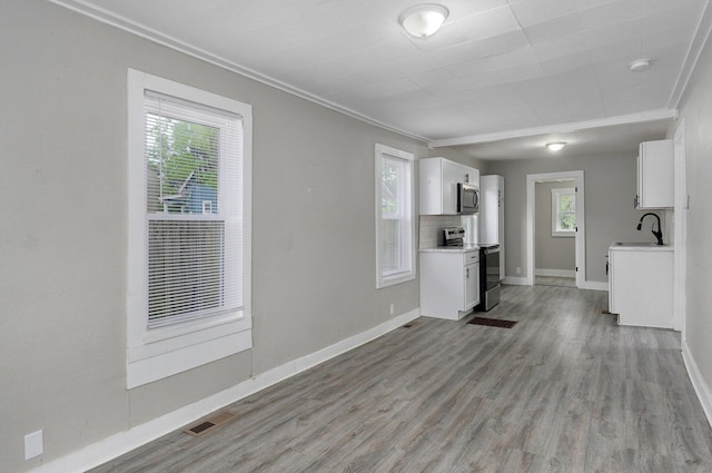 unfurnished living room with a sink, crown molding, light wood finished floors, and baseboards