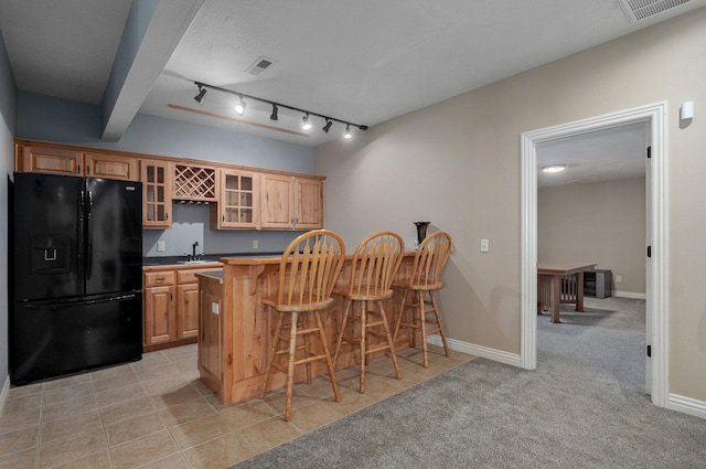 kitchen with black fridge with ice dispenser, a sink, a breakfast bar, glass insert cabinets, and a peninsula