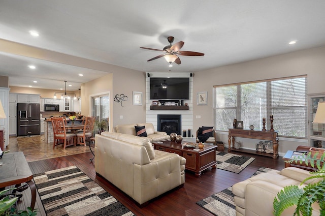 living area with a fireplace, a ceiling fan, dark wood finished floors, recessed lighting, and baseboards