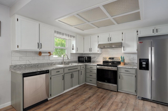 kitchen featuring stainless steel appliances, a sink, under cabinet range hood, dark wood finished floors, and backsplash