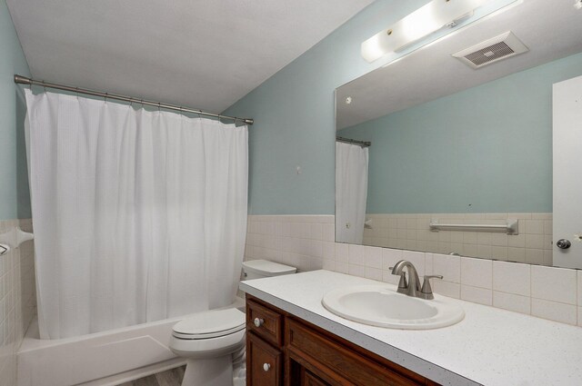 full bathroom with toilet, vanity, shower / tub combo with curtain, wainscoting, and tile walls