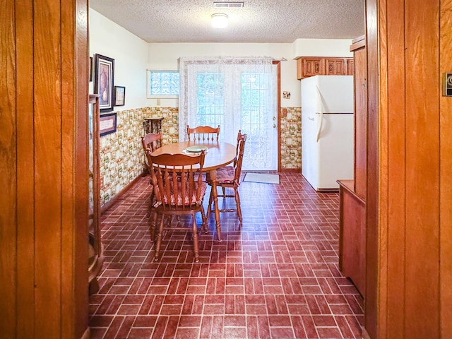 dining area featuring wainscoting, brick patterned flooring, and a textured ceiling