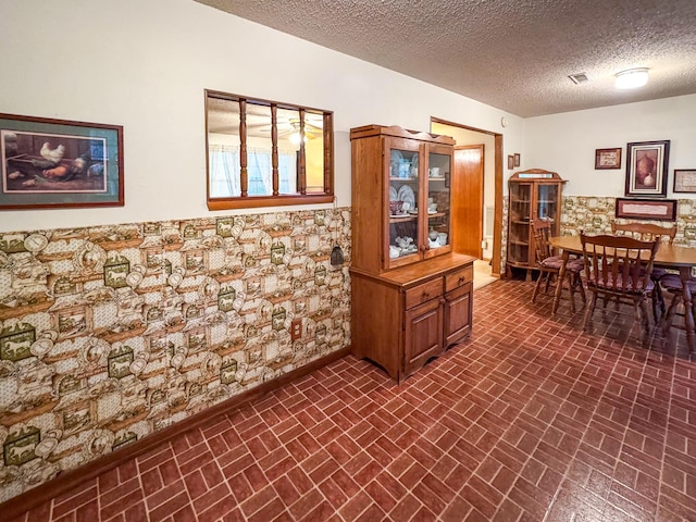 dining space featuring brick patterned floors, a textured ceiling, and baseboards