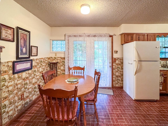dining space with wainscoting, brick patterned floors, plenty of natural light, and a textured ceiling