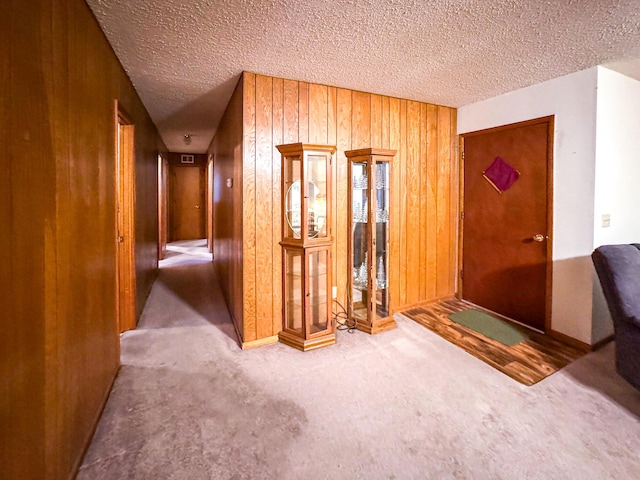 carpeted entryway featuring wooden walls and a textured ceiling