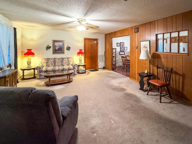 living room with carpet flooring, a ceiling fan, wood walls, and a textured ceiling