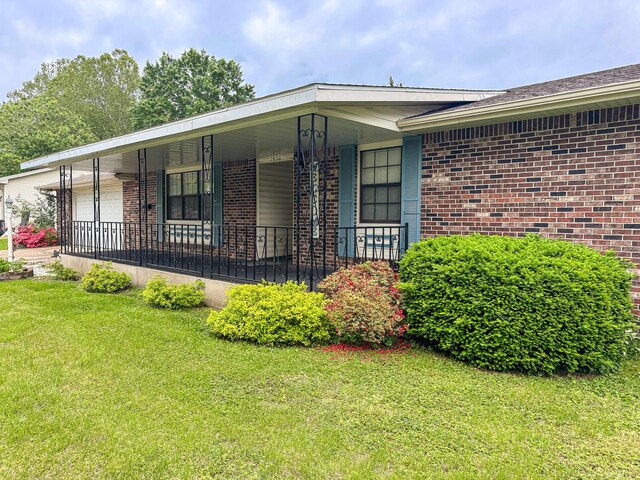 view of front of house with brick siding, a garage, a front lawn, and covered porch
