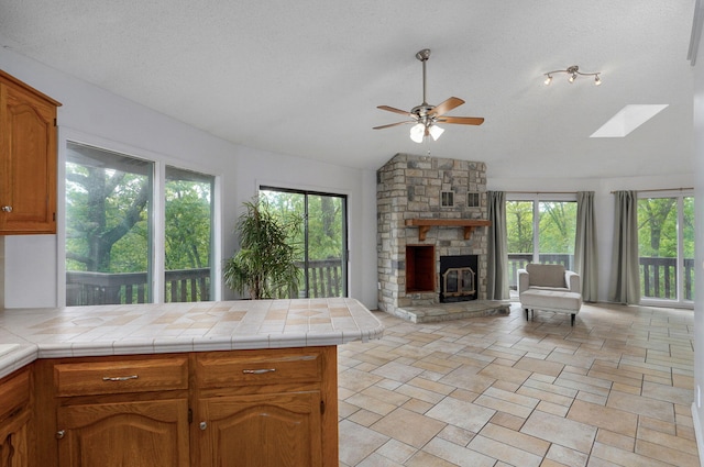 kitchen featuring lofted ceiling, open floor plan, a ceiling fan, a stone fireplace, and a peninsula