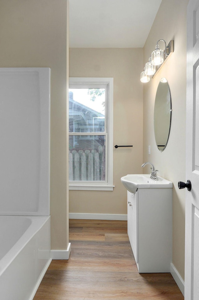 bathroom featuring wood finished floors, vanity, baseboards, and a bath