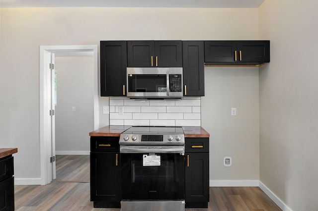kitchen featuring stainless steel appliances, dark cabinetry, wood finished floors, and baseboards