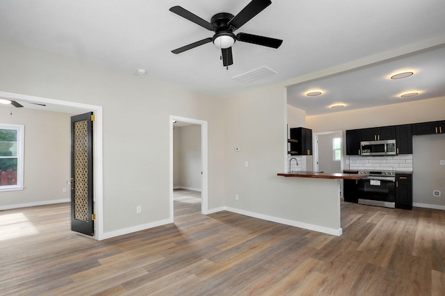 kitchen with ceiling fan, stainless steel appliances, dark cabinets, light wood-style flooring, and open floor plan