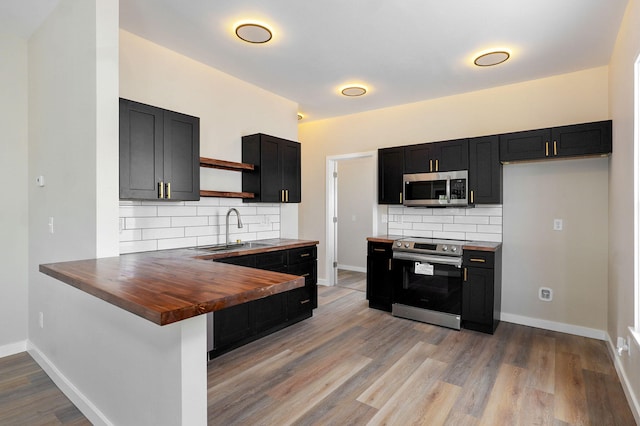 kitchen featuring stainless steel appliances, open shelves, a sink, wooden counters, and tasteful backsplash