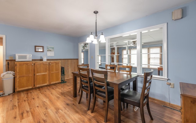 dining room with light wood-type flooring, wainscoting, a chandelier, and wood walls