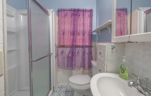 bathroom featuring a sink, a stall shower, tile walls, and toilet