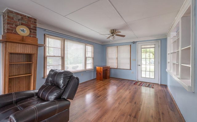 living area with a ceiling fan, wood finished floors, and ornamental molding