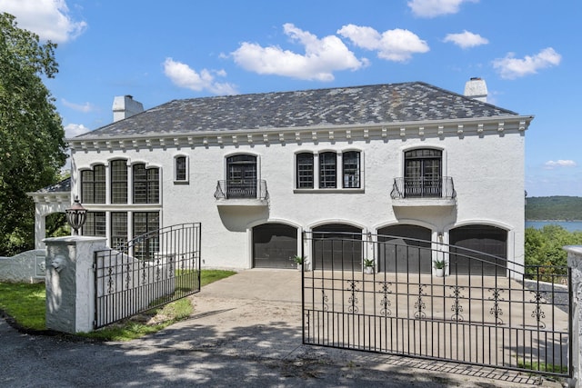 view of front of home with a balcony, an attached garage, concrete driveway, a chimney, and a fenced front yard