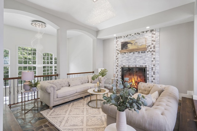 living area featuring a stone fireplace, wood finished floors, recessed lighting, baseboards, and arched walkways